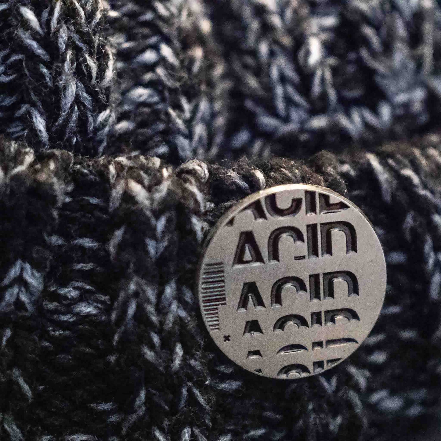 Antique silver with black enamel acid house pin badge on a wooly hat