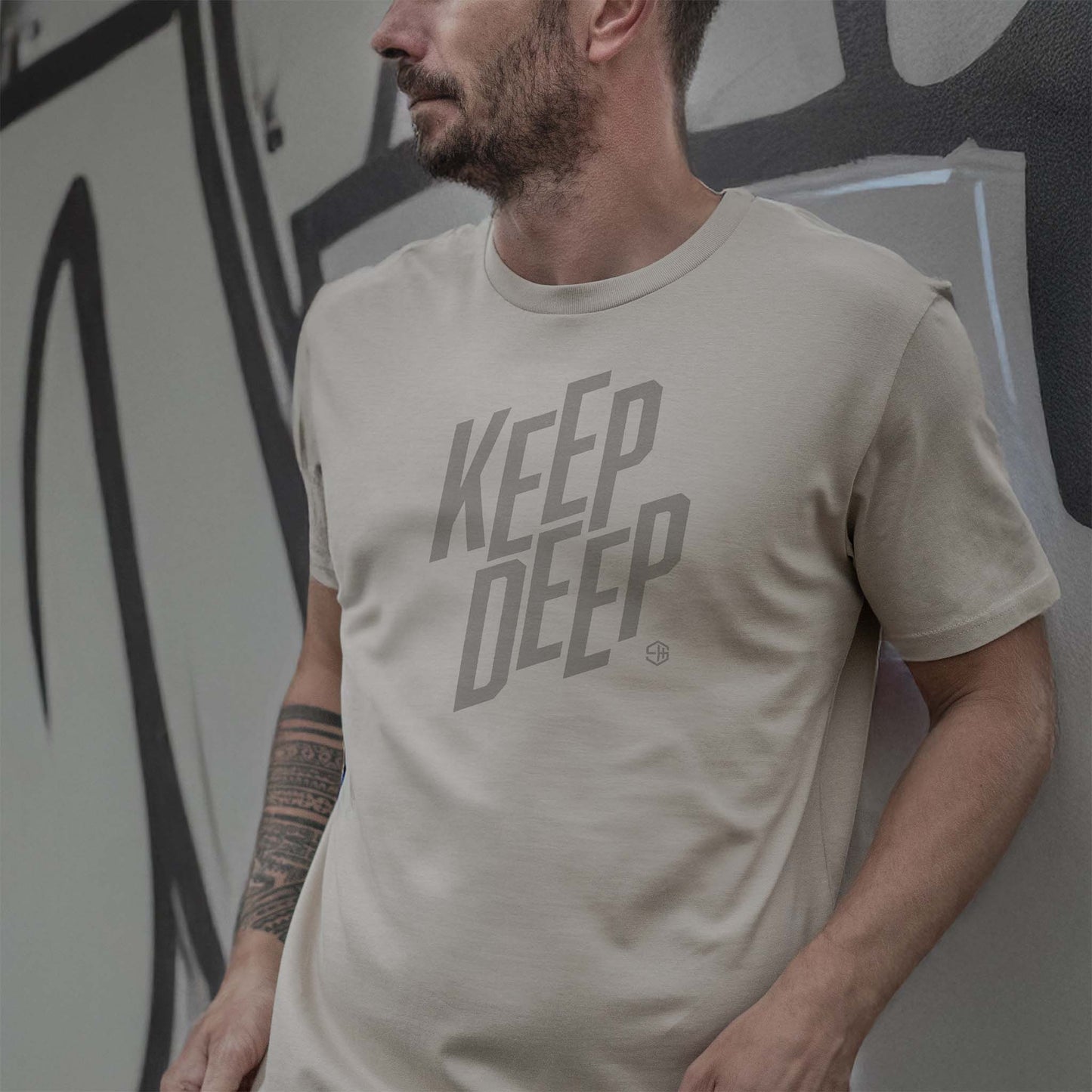 Man wearing a grey deep house t-shirt with 'KEEP DEEP' text against a graffiti wall.