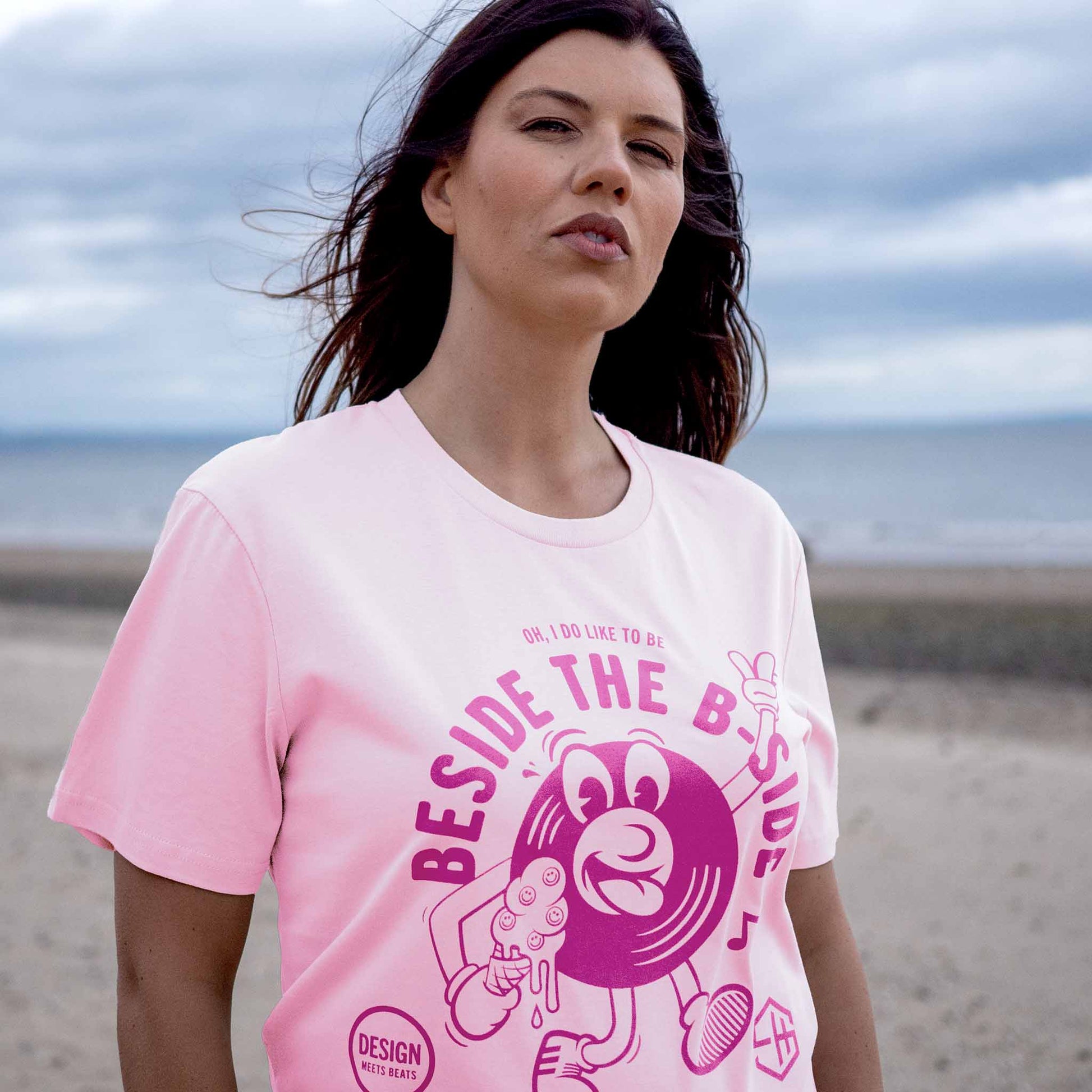 Woman wearing a pink summer vibes t-shirt with a graphic design on a beach