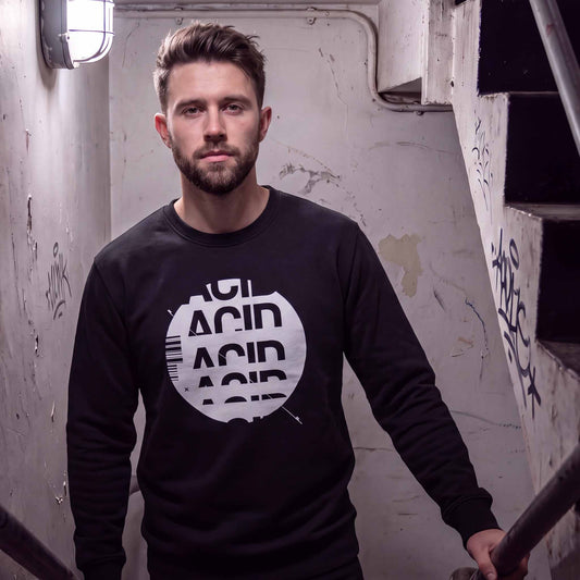 Man wearing a black acid house sweatshirt with white ACID DROP screen print, standing in a stairwell.
