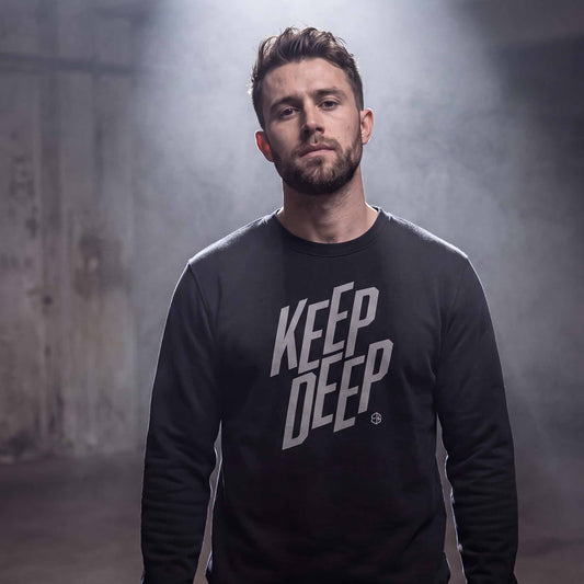 Man wearing a black deep house sweatshirt with KEEP DEEP silver-grey type in a warehouse.