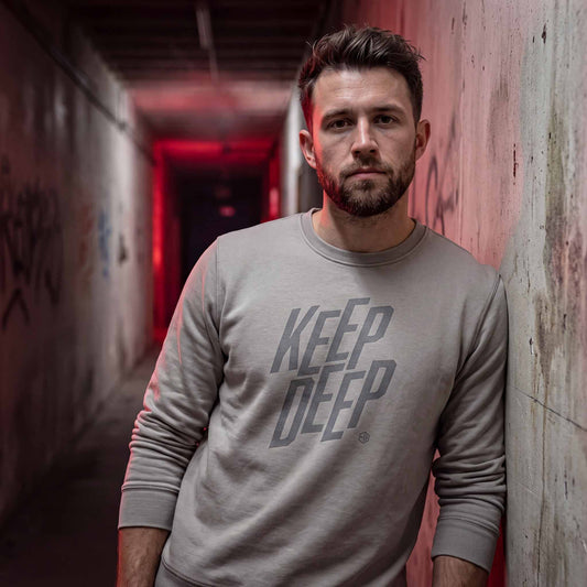 Man wearing a grey deep house sweatshirt with KEEP DEEP silver-grey type in a warehouse.